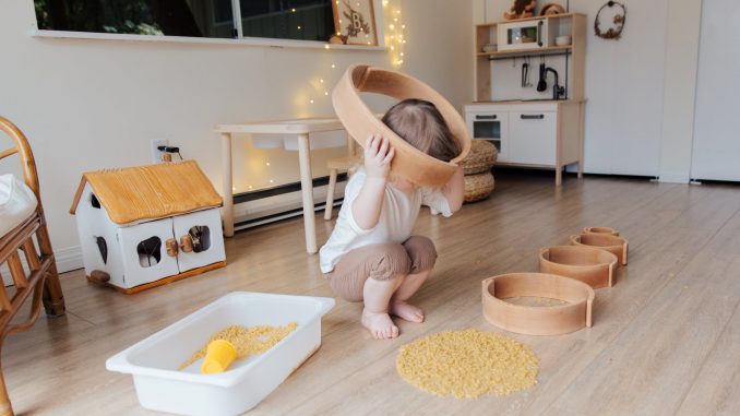 faceless toddler playing with wooden shapes of different size and pasta at home while putting biggest shape on