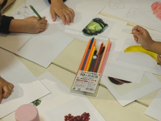 unrecognizable preschool ethnic children drawing on papers during class