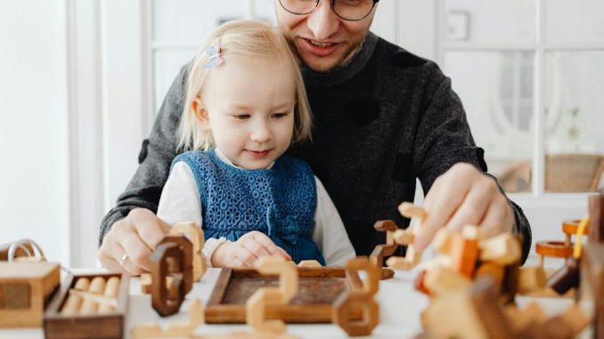 a man talking to his daughter while playing wooden toys on the table